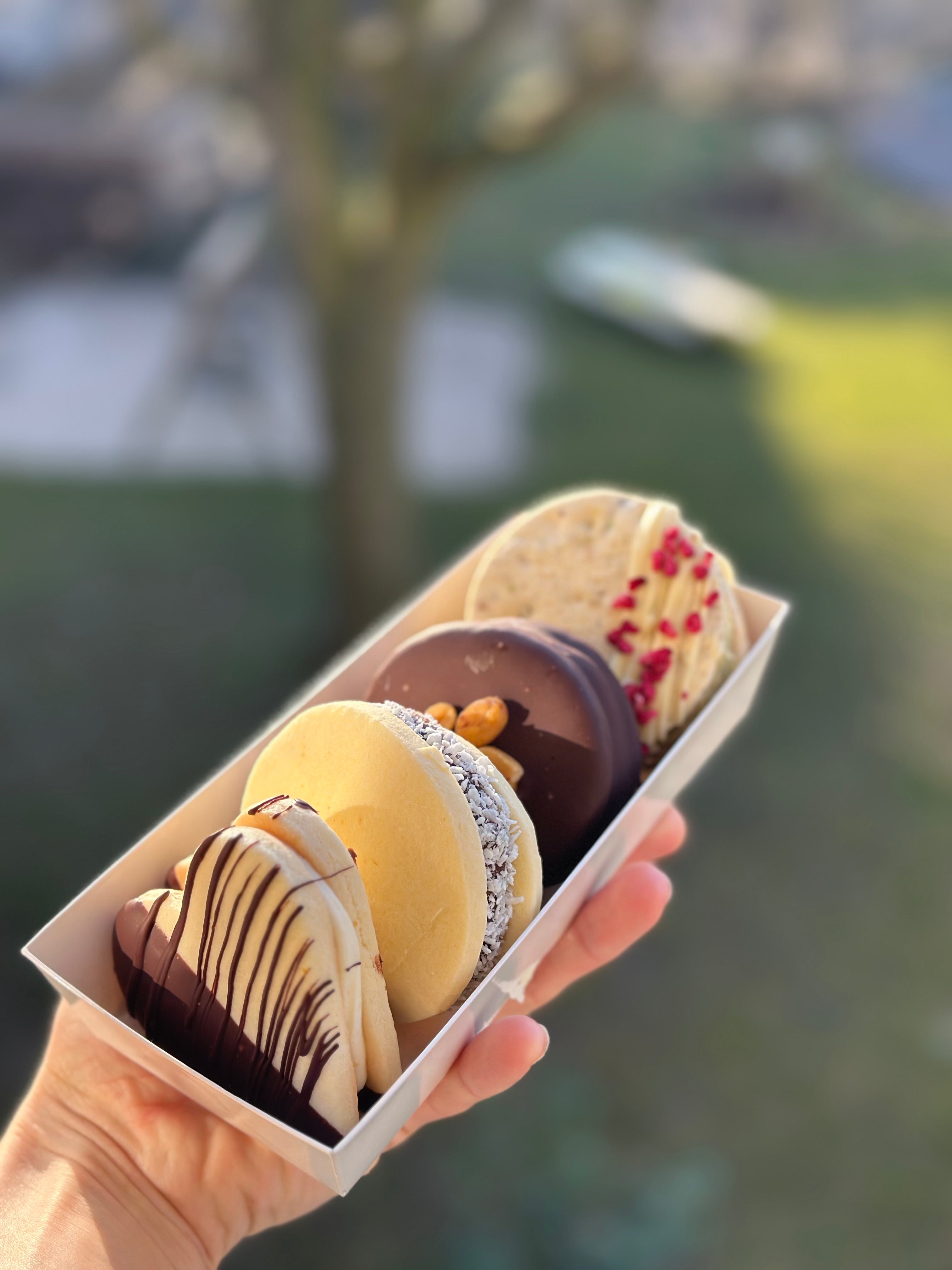 Three handmade gluten-free alfajores in white chocolate, dark chocolate, and pistachio coatings, the Argentine classic baked by Gluten Tag in Copenhagen.