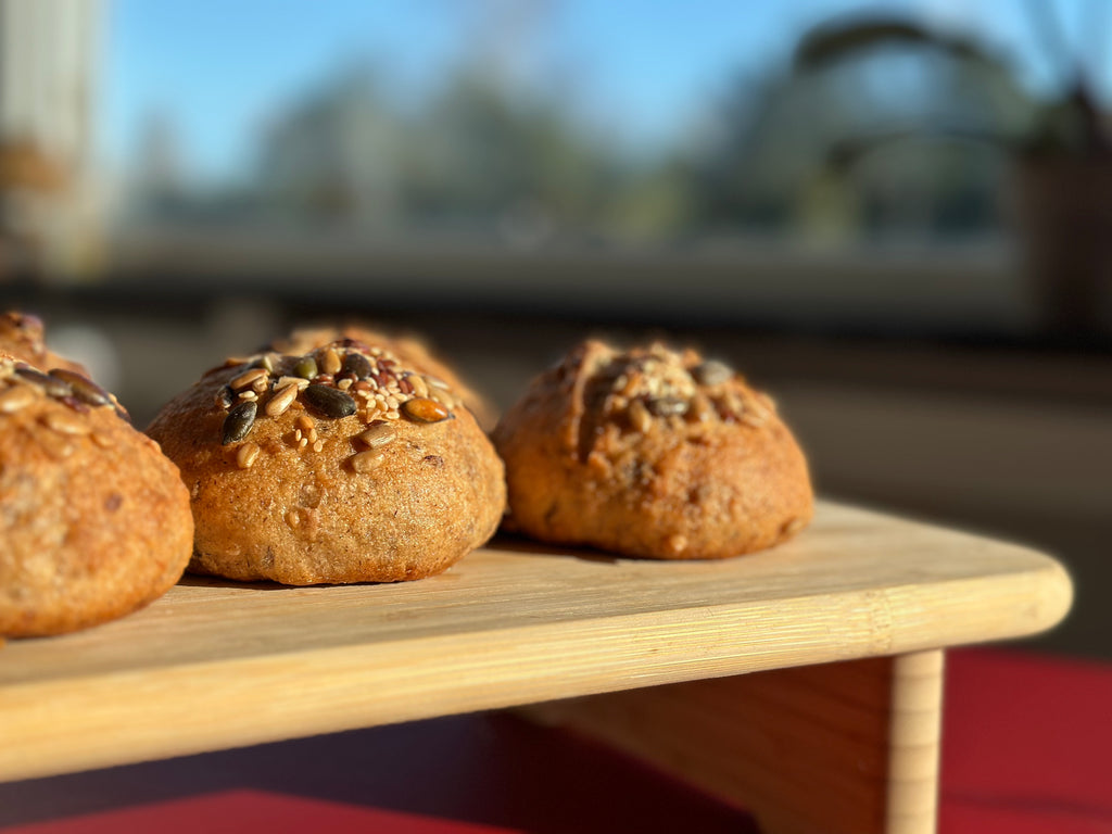 Gluten-free vegan boller with mixed seeds on a wooden board, the Danish bread buns baked by Gluten Tag in Copenhagen.